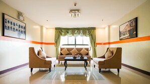 A hotel lobby with a sofa set, two armchairs, a coffee table, and a large window with green curtains.