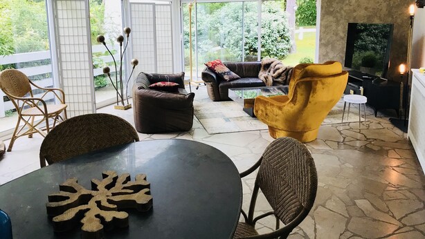 A spacious living area with a large glass door leading to a balcony, a black leather sofa, a yellow armchair, and a dining table with a decorative centerpiece. - Beautiful architect house in the forest of Le Touquet (Le Touquet-Paris-Plage)