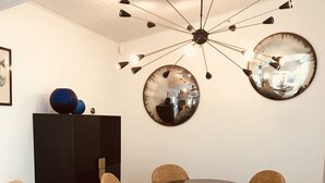 A dining area with a round table surrounded by wicker chairs, a black cabinet, and a large mirror on the wall. - Beautiful architect house in the forest of Le Touquet (Le Touquet-Paris-Plage)