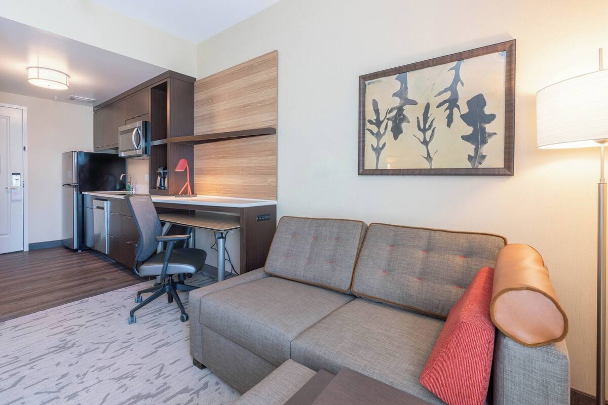 A modern living room with a sofa, a desk, and a kitchen area.