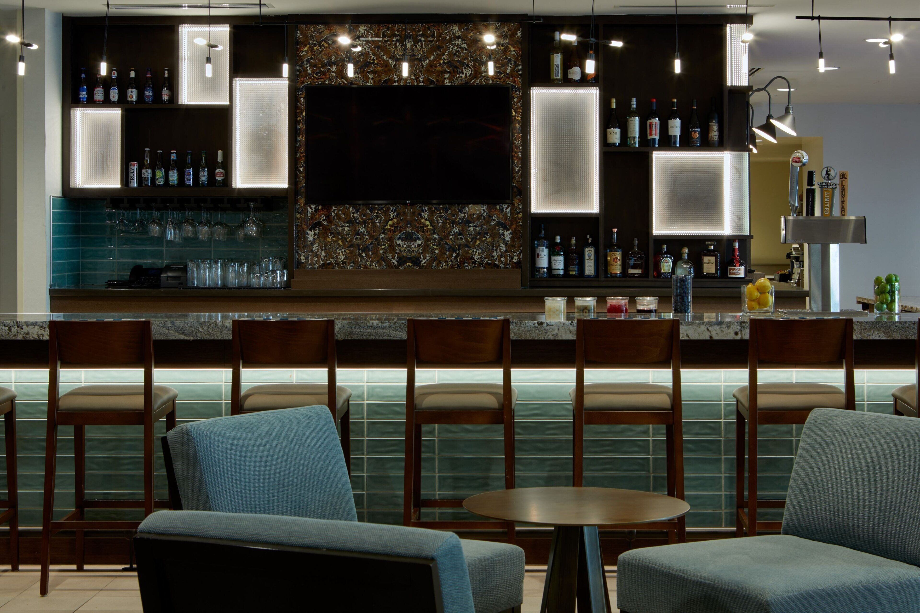 A bar area with a flat-screen TV, bar stools, and a variety of bottles and glasses.