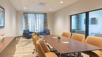 A conference room with a long table, six chairs, a blue sofa, and a large window with curtains.
