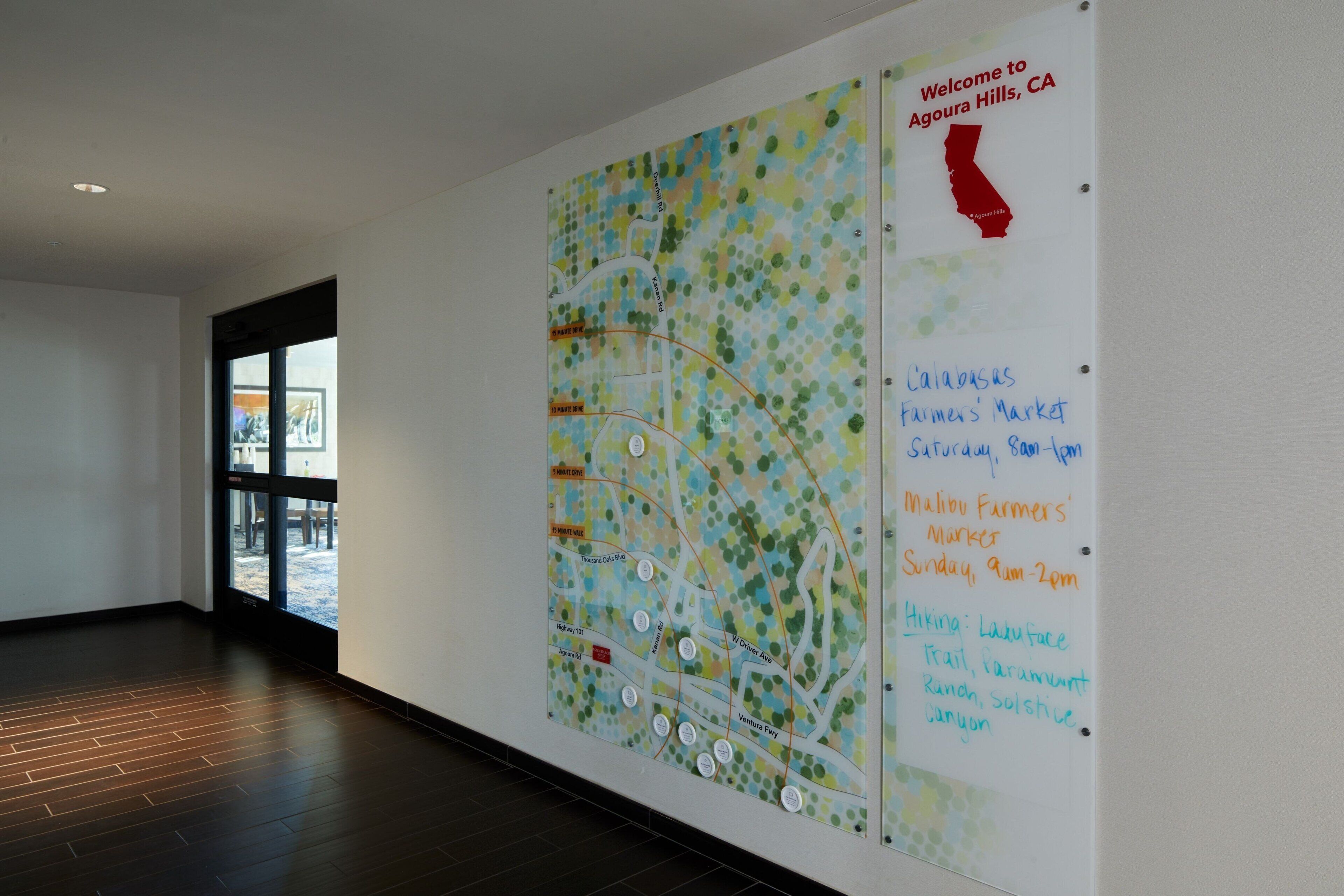 Mapa a la paret amb un cartell de benvinguda a Agoura Hills, CA, i una llista d'atracions i mercats locals.