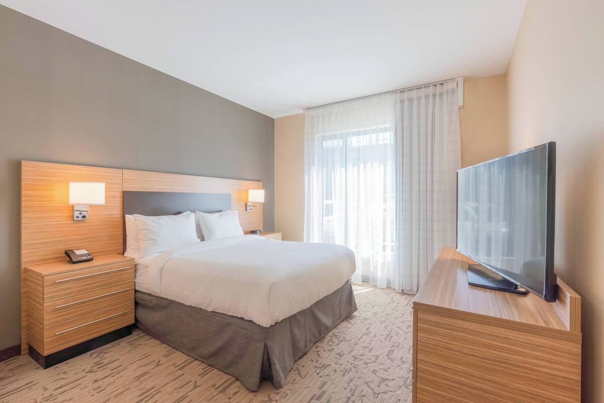 A hotel room with a bed, bedside tables, a TV, and a window with curtains.