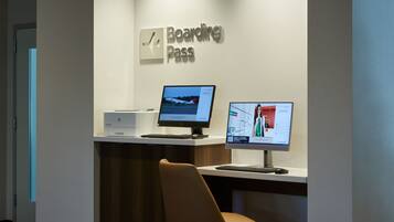 A reception desk with a 'Boarding Pass' sign, two computer monitors, a printer, and a brown leather chair.