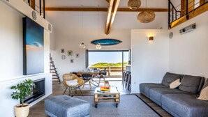 A modern living room with a sofa, ottoman, and coffee table, a dining area with chairs, and a staircase leading to an upper level. - Villa Oceana exceptional property sea view from every room (Ondres)