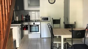 A compact kitchen with modern appliances, a dining area with a table and chairs, and a staircase leading to an upper level. - The Vieux Fossés duplex (Romorantin-Lanthenay)