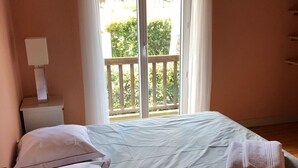 A bedroom with a bed, pillows, a nightstand with a lamp, and a balcony with a railing. - Beautiful style house near the golf course (Soorts-Hossegor)