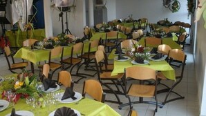 Een eetgedeelte met meerdere tafels gedekt voor een maaltijd, elk met groene tafelkleden, stoelen en netjes opgemaakte zitplaatsen.