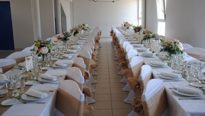 Een lange feesttafel, gedekt met witte tafelkleden, gouden linten en bloemstukken.