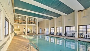 Una piscina interior con vista despejada al área de la piscina, una zona de estar con mesas y sillas, y un nivel superior con barandilla.
