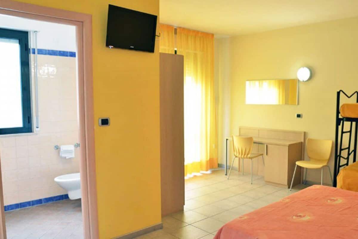 A hotel room with a bed, a desk, a chair, a toilet, and a TV.
