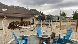 Un'area salotto esterna con poltrone Adirondack blu, un braciere in pietra e un'amaca.