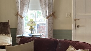 A room with a red sofa, a lamp, and a window with floral curtains. - Clara's house at Homestead B&B (Dripping Springs,)