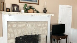 A living room with a stone fireplace, a television on a wooden stand, a patterned rug, and a painting above the fireplace. - Clara's house at Homestead B&B (Dripping Springs,)