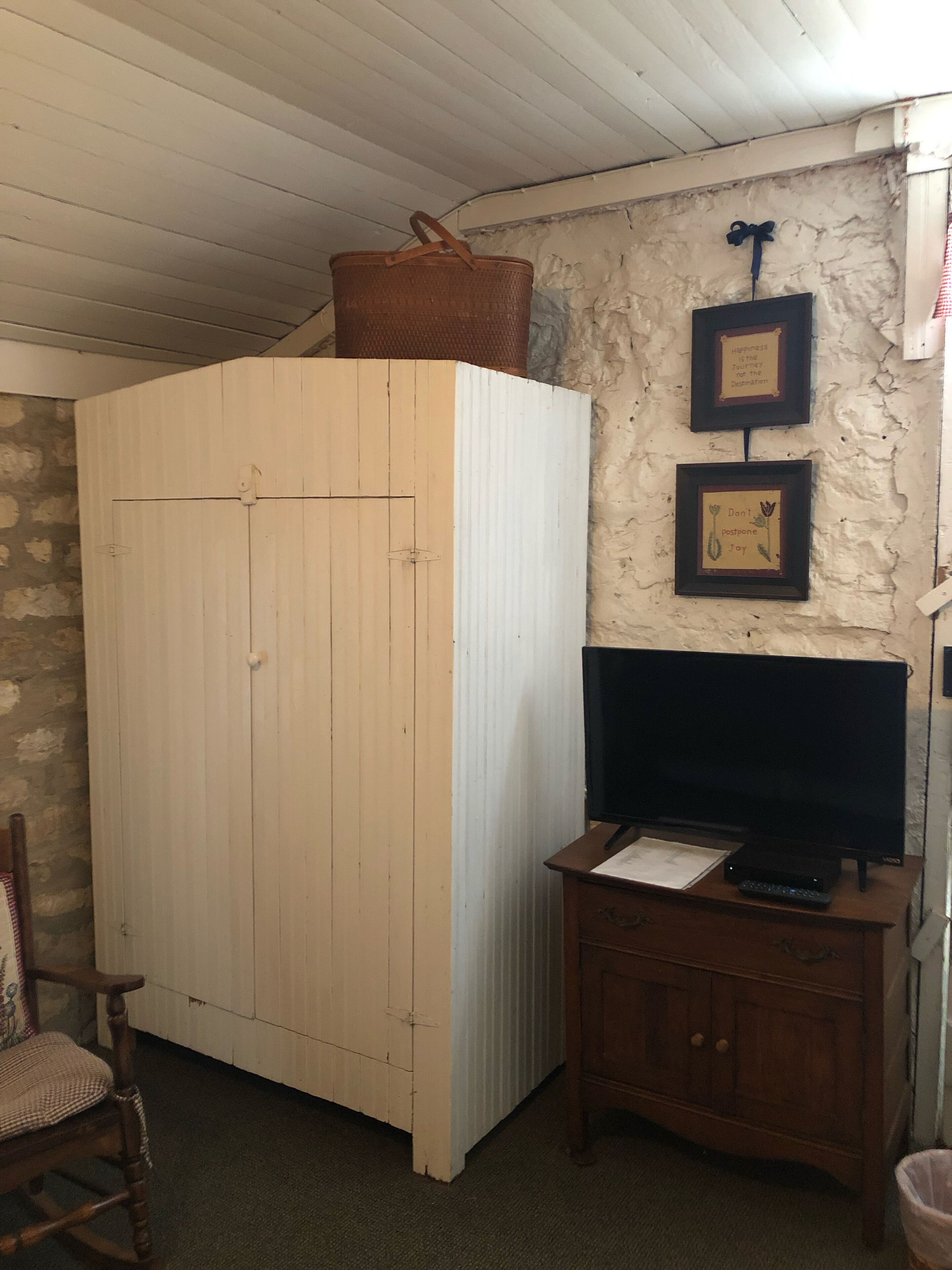 A room with a wooden wardrobe, a television on a wooden cabinet, and two framed pictures on the wall.