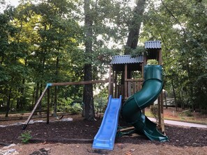 Explore the playground in our wooded park setting, featuring a playhouse and a green slide.