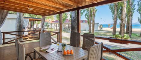 Un espace extérieur abrité, avec une table en bois, des chaises et une vue sur la plage.