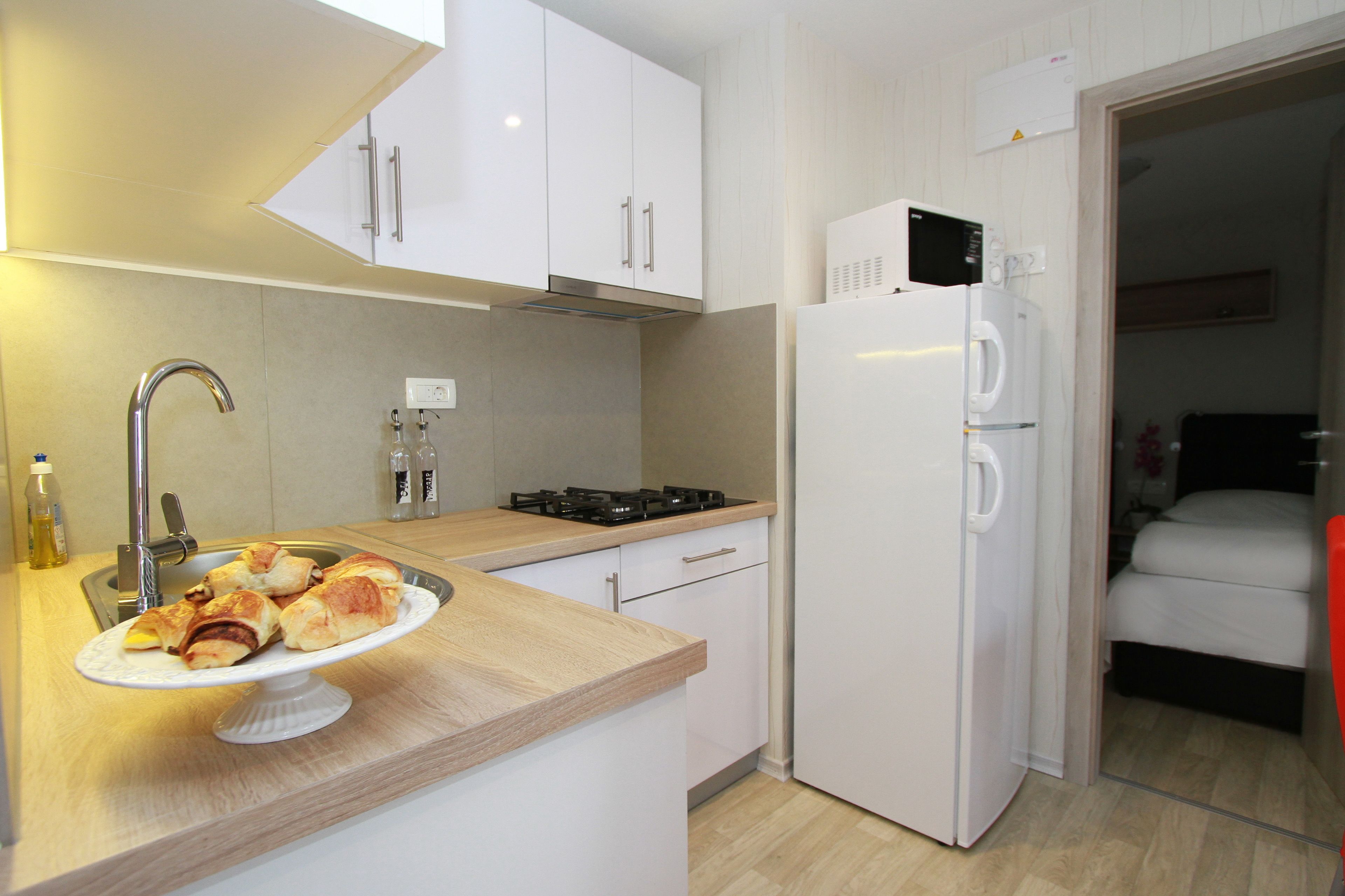 Une cuisine de taille réduite, équipée d’un évier, d’une cuisinière et de meubles blancs.