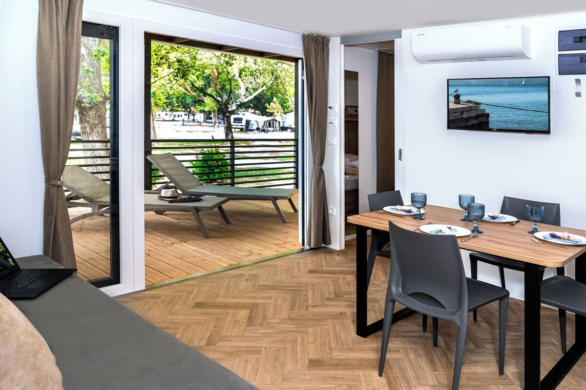 Una habitación moderna con una mesa de comedor de madera, sillas grises y una computadora portátil sobre un sofá gris.