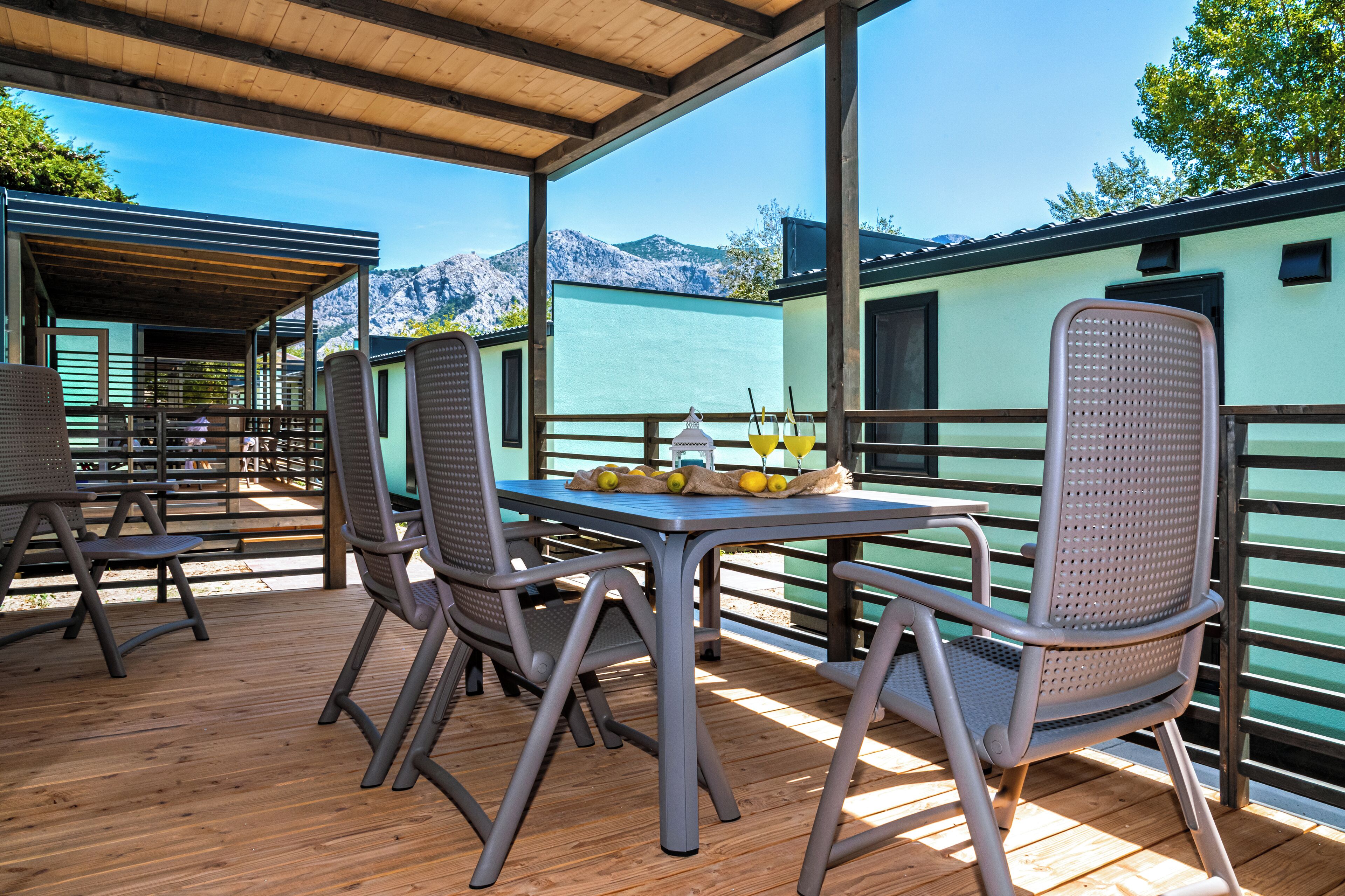 A covered outdoor seating area with a table and chairs, overlooking a mountainous landscape.