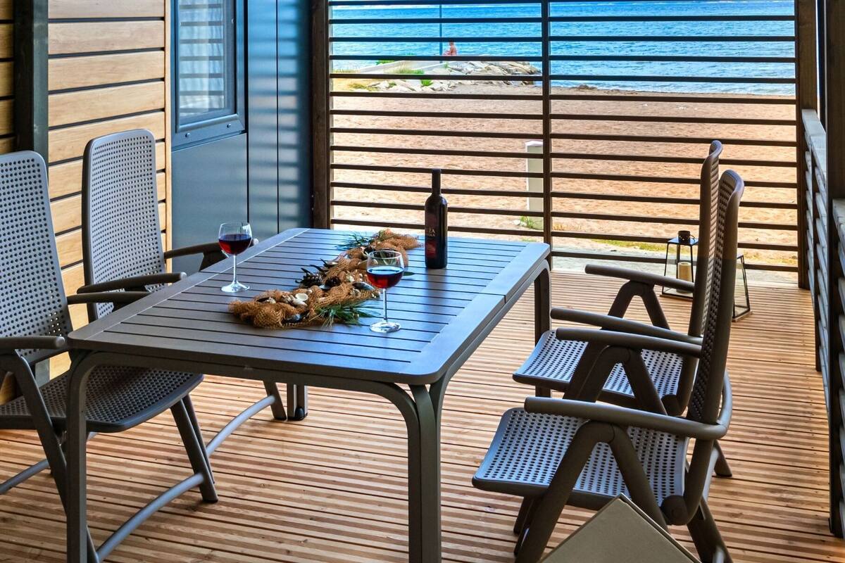 Un espacio de comedor al aire libre con una mesa, sillas, una botella de vino y una copa de vino tinto.