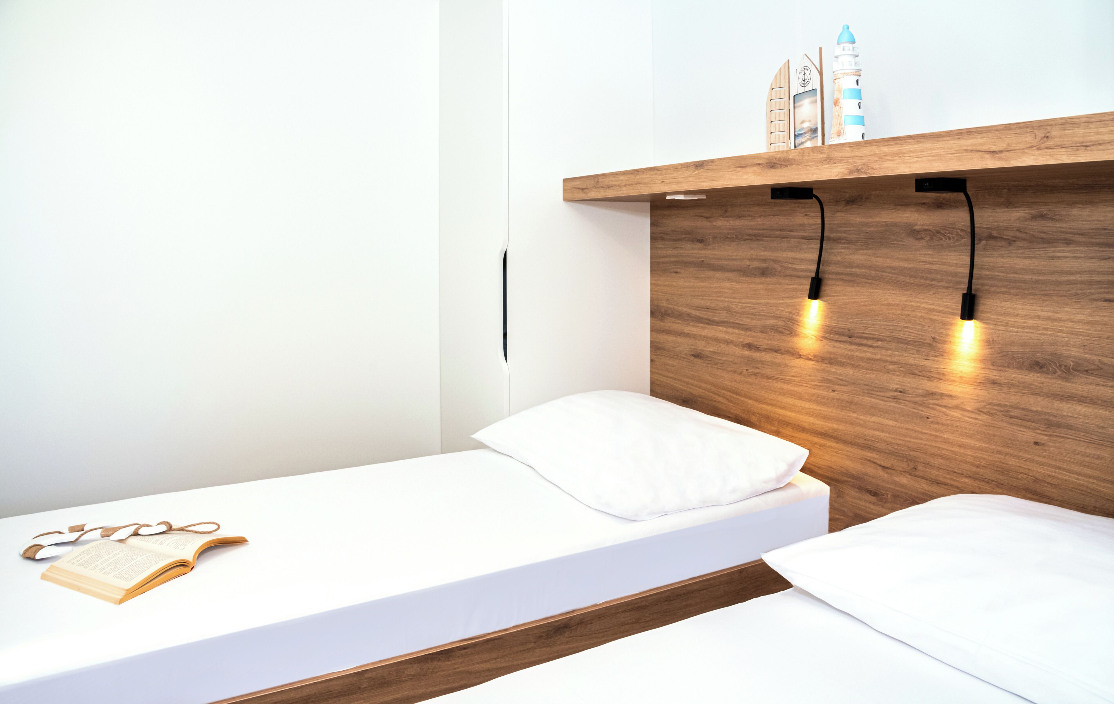 Una habitación de hotel moderna con cabecera de madera, cama blanca y estante con adornos.