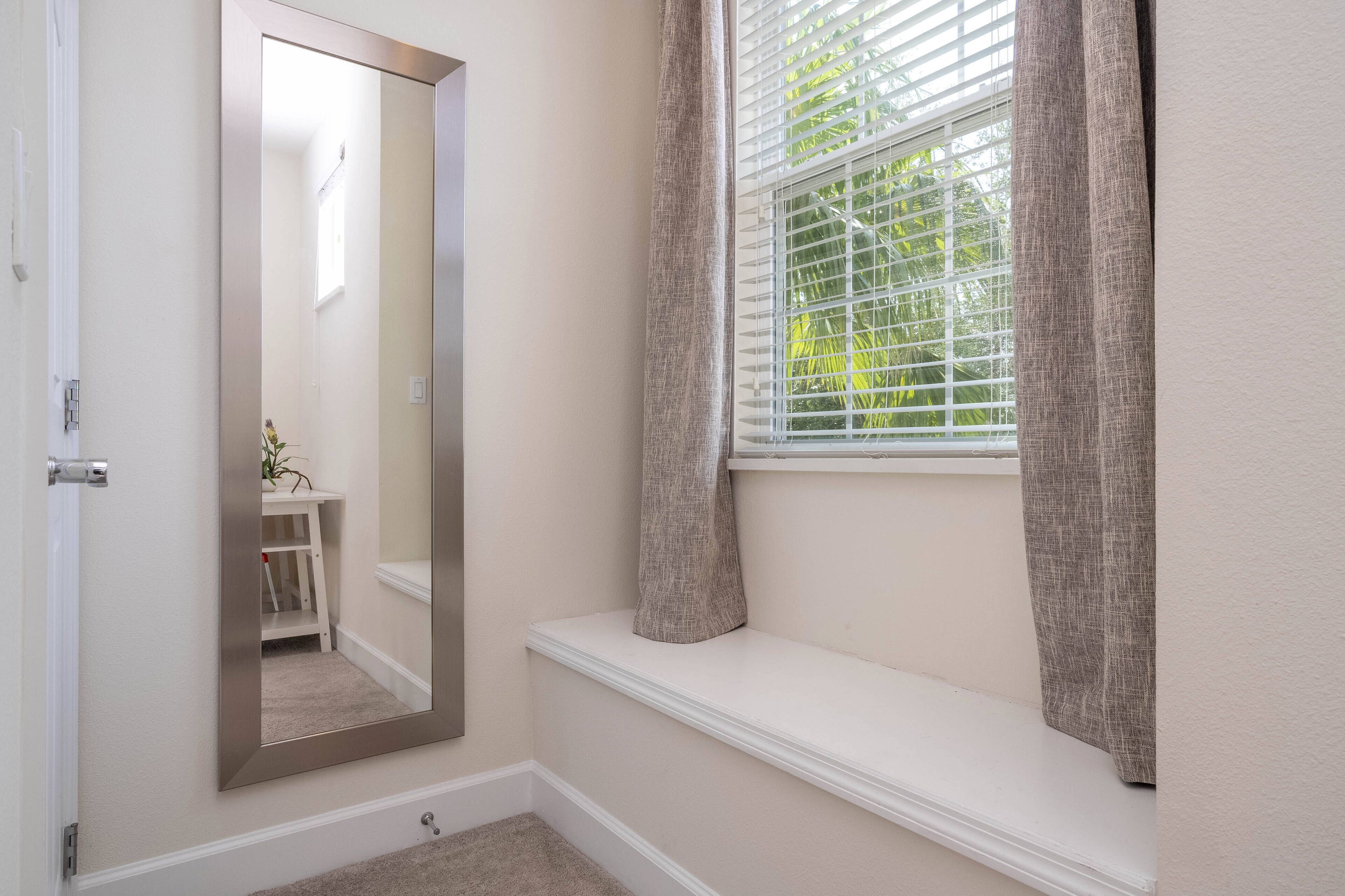 A bathroom with a large mirror, a window with blinds, and a bench.