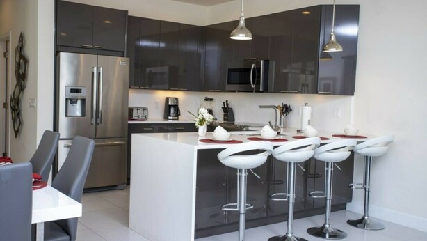 Una cocina moderna con armarios oscuros, electrodomésticos de acero inoxidable y una isla central con taburetes de bar.