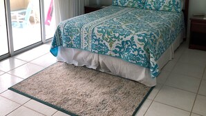 Un dormitorio con cama, mesita de noche, lámpara y vistas al exterior.