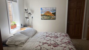A bedroom with a bed, a window with a plant, a painting on the wall, and a door. - Beautiful private 2 bedrooms/1 bathroom near campus (Boulder)