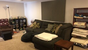 A living room with a sectional sofa, ottoman, and a small wooden table. There is a bookshelf with storage bins and a lamp. - Beautiful private 2 bedrooms/1 bathroom near campus (Boulder)
