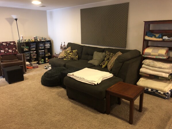 A living room with a sectional sofa, ottoman, and a small wooden table. There is a bookshelf with storage bins and a lamp. - Beautiful private 2 bedrooms/1 bathroom near campus (Boulder)
