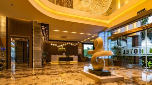 A hotel lobby with a reception desk, a large abstract sculpture, and a glass wall offering a view of the outdoors. - Zen Riverside Hotel & Residences (Hai Phong)