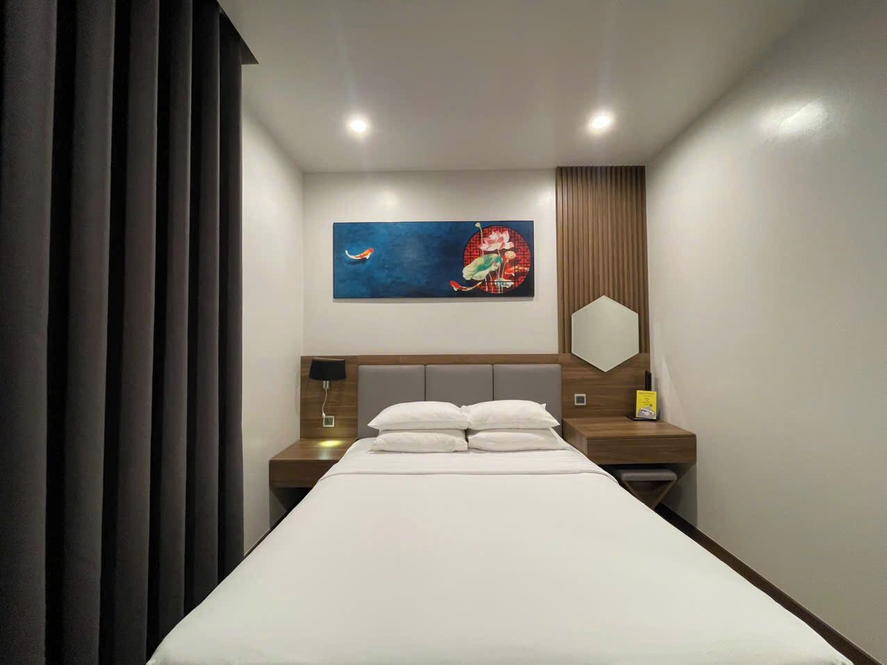Camera d'albergo moderna con un letto grande, un comodino con una lampada, uno specchio a parete e un quadro sopra il letto.