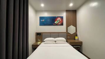 Camera d'albergo moderna con un letto grande, un comodino con una lampada, uno specchio a parete e un quadro sopra il letto.
