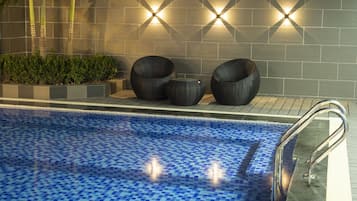 A swimming pool with blue mosaic tiles, surrounded by a tiled wall with geometric patterns and wall-mounted lights.