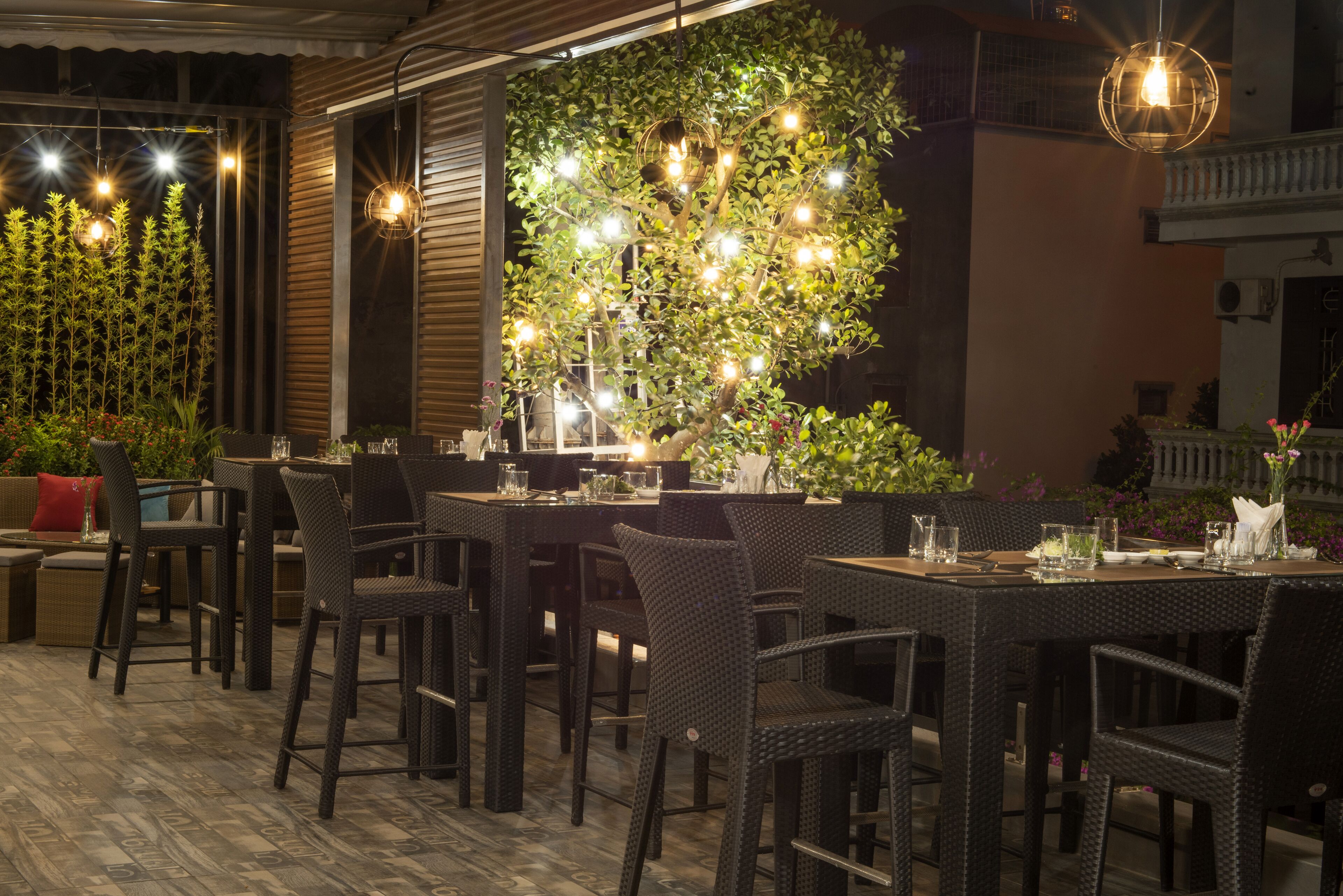 An outdoor dining area with wicker furniture and a tree illuminated by string lights.