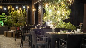 An outdoor dining area with wicker chairs and tables, surrounded by potted plants and illuminated by string lights. - Zen Riverside Hotel & Residences (Hai Phong)