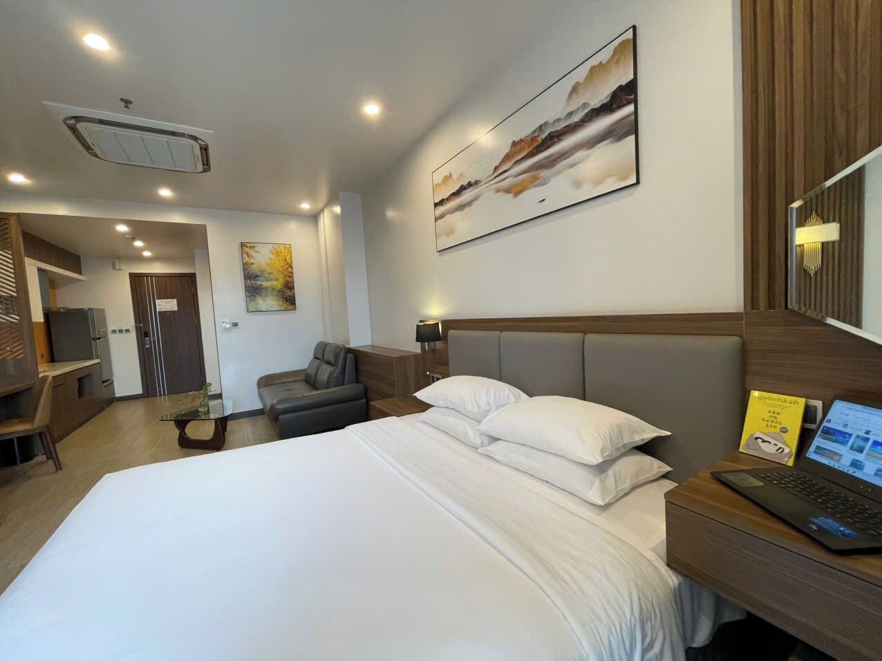 Una camera d'albergo con un letto, una scrivania con un portatile, una sedia, un divano, un quadro appeso al muro e una porta che dà su un'altra stanza.