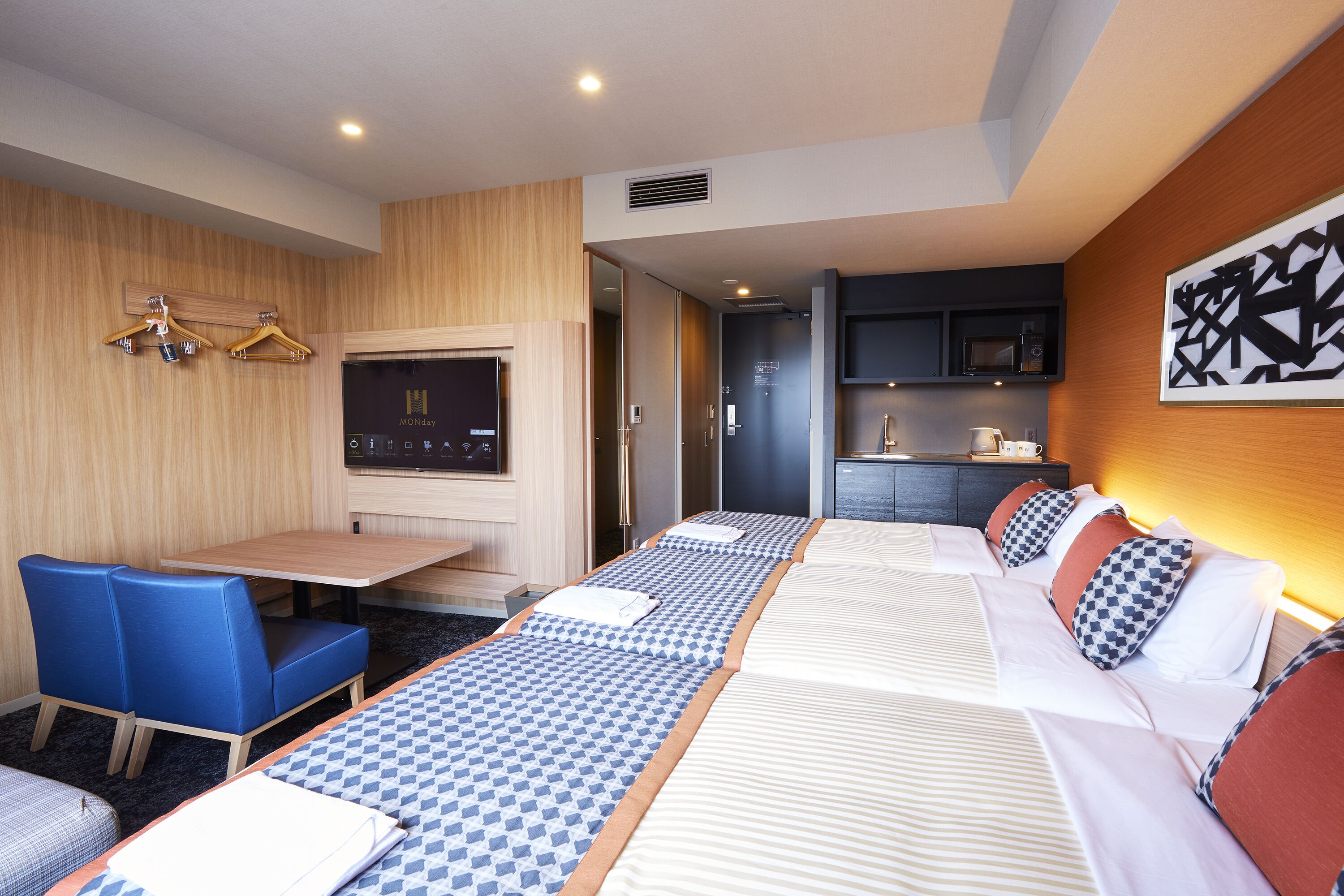 A hotel room with a sofa bed, a small table, a TV, and a kitchenette.