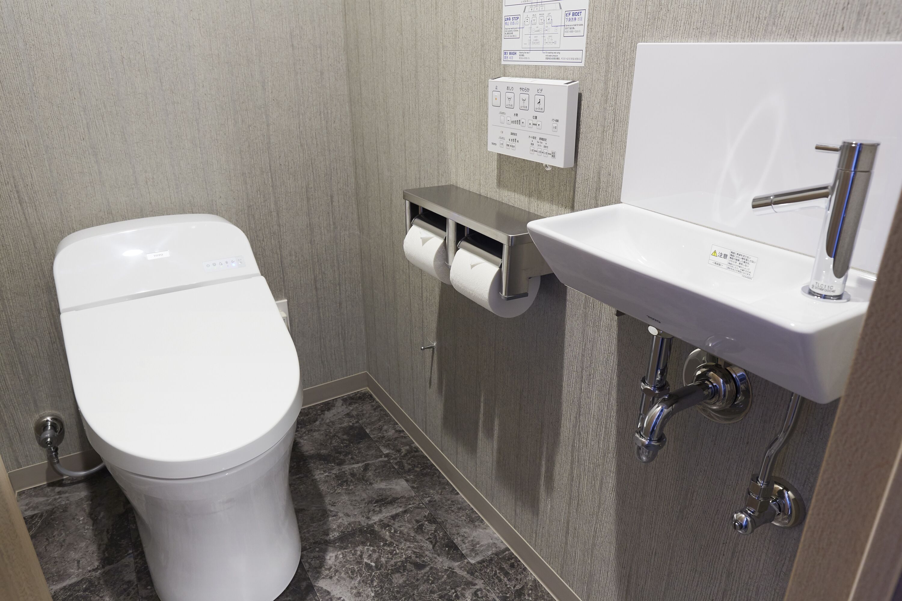 Une salle de bain équipée de toilettes, d’un distributeur d’essuie-tout et d’un lavabo avec un robinet.
