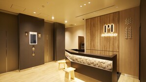 A modern reception area with a wooden reception desk, a small wooden stool, and a wall-mounted sign with the word "MONday". - hotel MONday Asakusa (Tokyo)