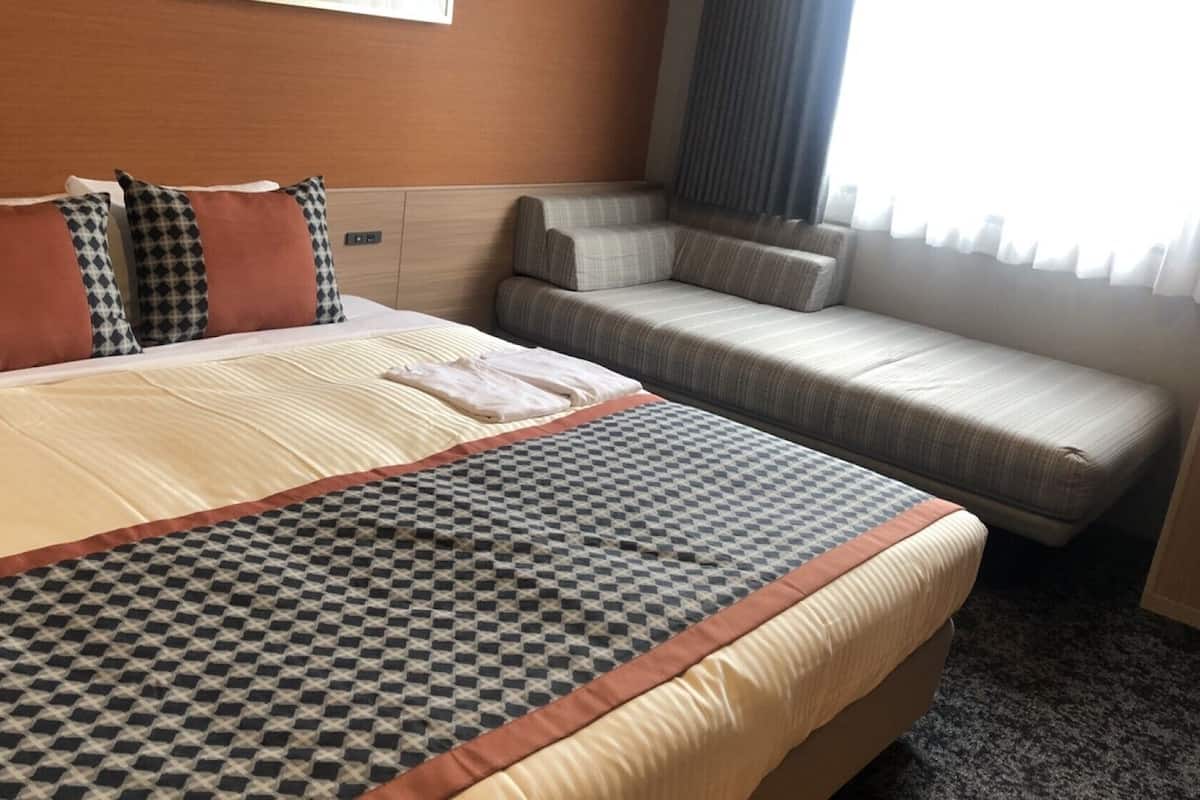 A hotel room with a large bed, a sofa, and a window with curtains.