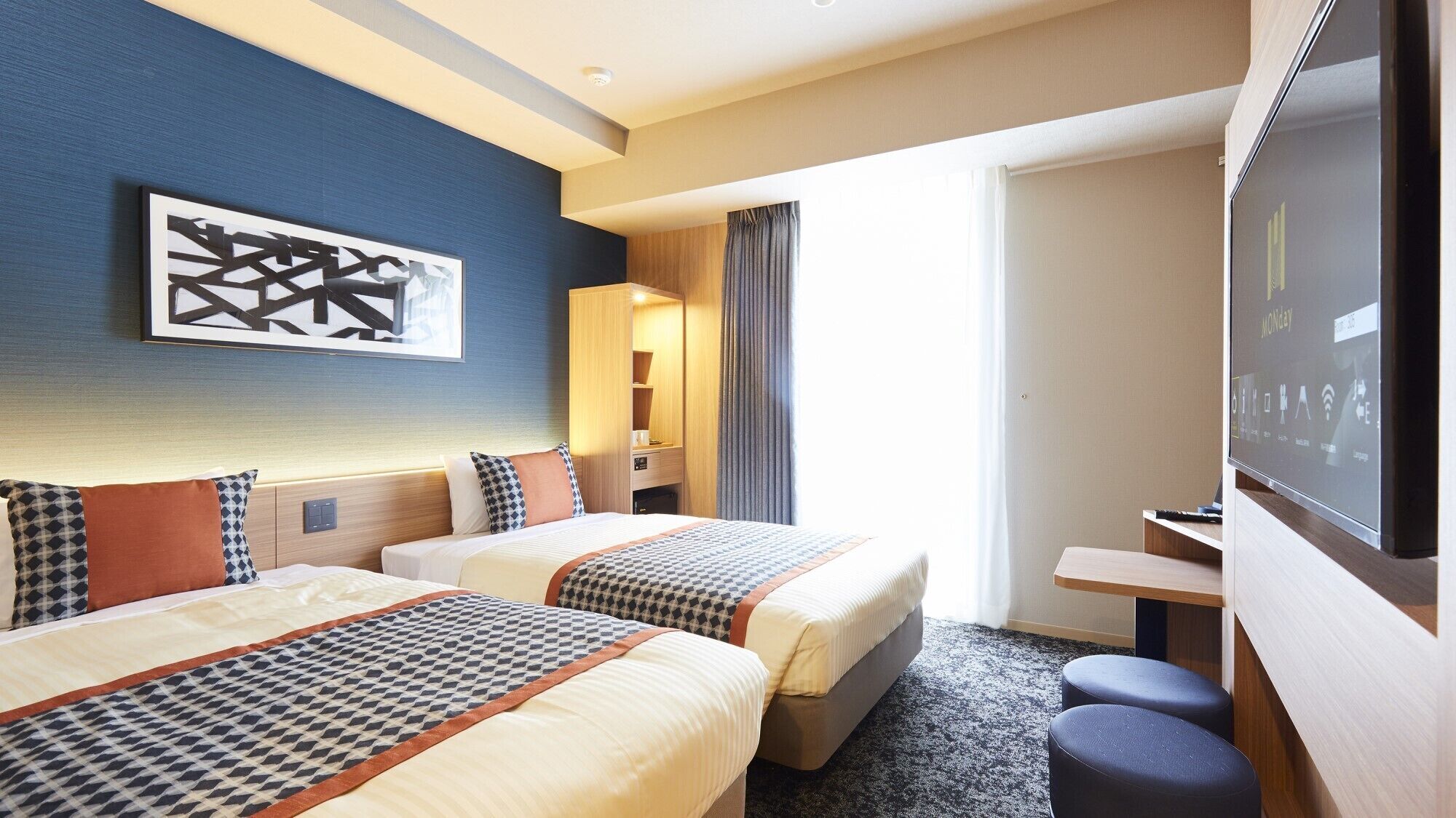 A hotel room with two beds, a TV, a desk, and a large window.