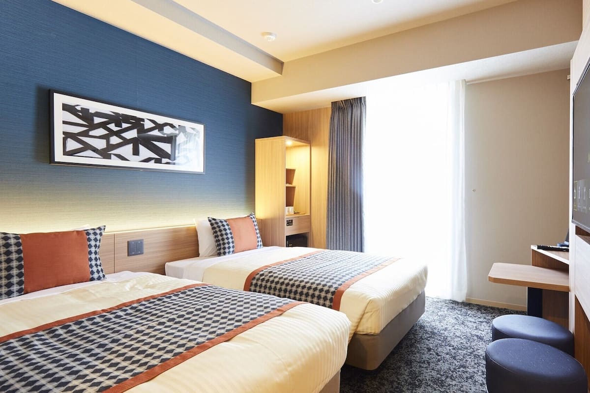 A hotel room with two beds, a TV, a desk, and a large window.