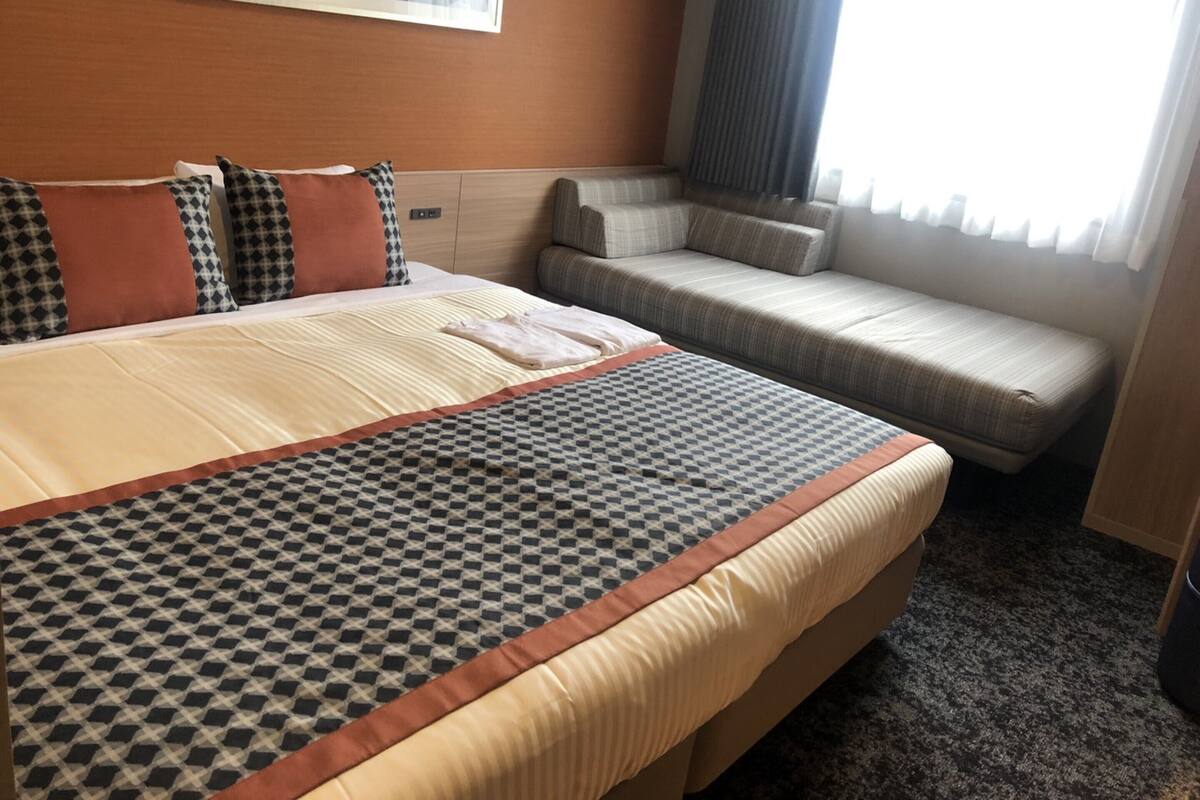 A hotel room with a large bed, a sofa bed, a wall-mounted artwork, and a window with curtains.