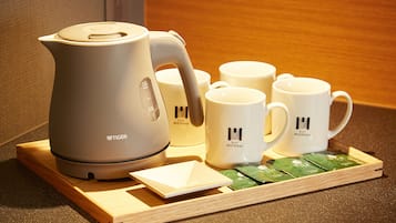 A tea set with a kettle, cups, and tea packets on a wooden tray.