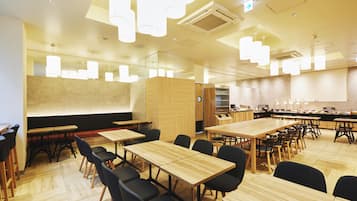 Un comedor amplio con varias mesas de madera y sillas negras, una pantalla grande para presentaciones e iluminación colgante moderna.