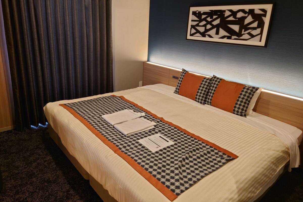 A hotel room with a large bed, a headboard, a wall-mounted artwork, and a window with curtains.
